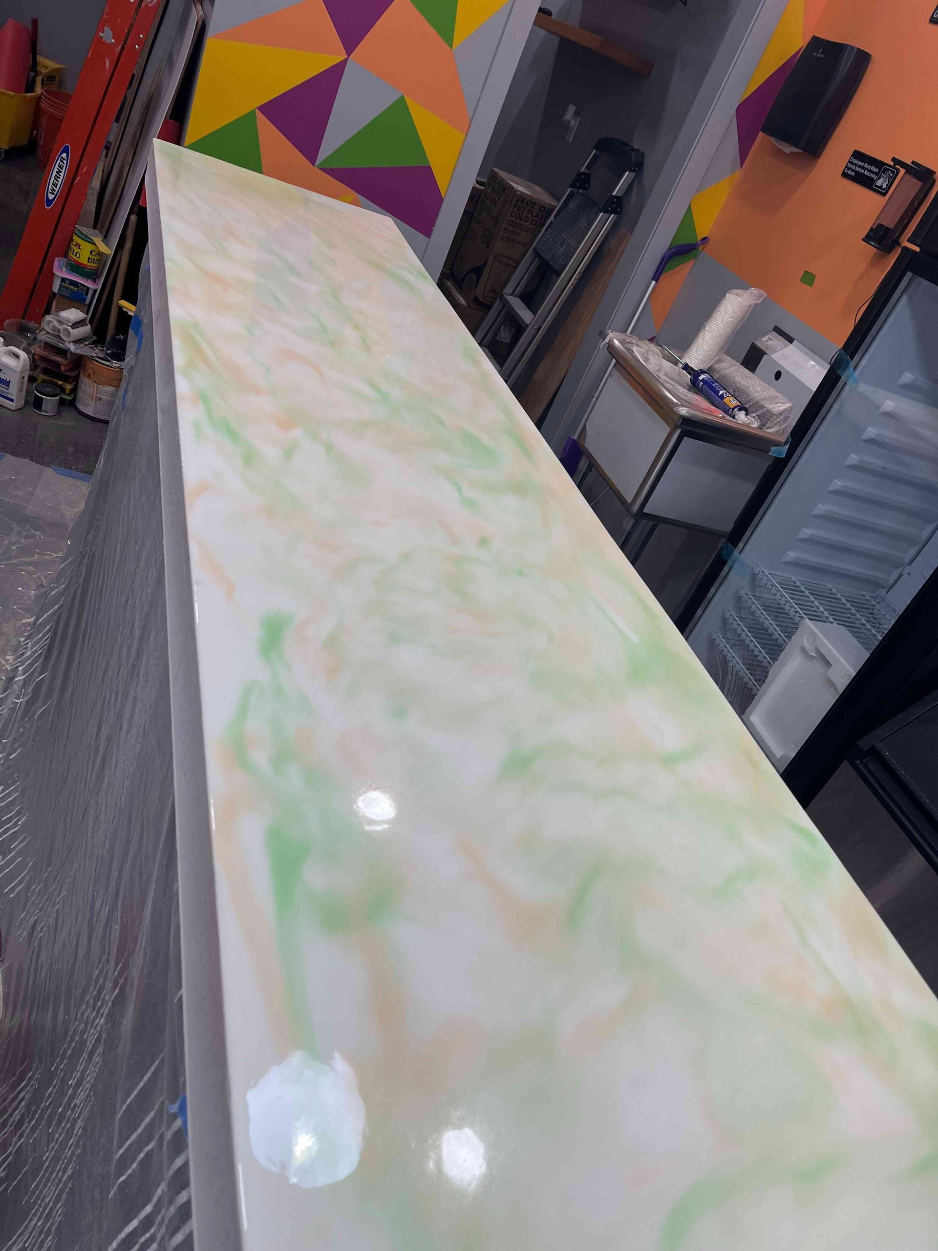 A long, white countertop with green and tan swirls in a brightly lit room.