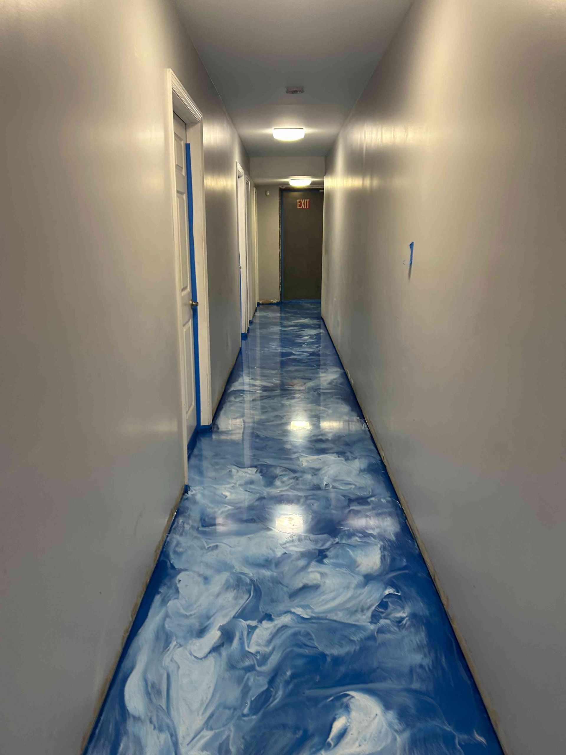 Long hallway with blue and white epoxy floor, gray walls, and doors.