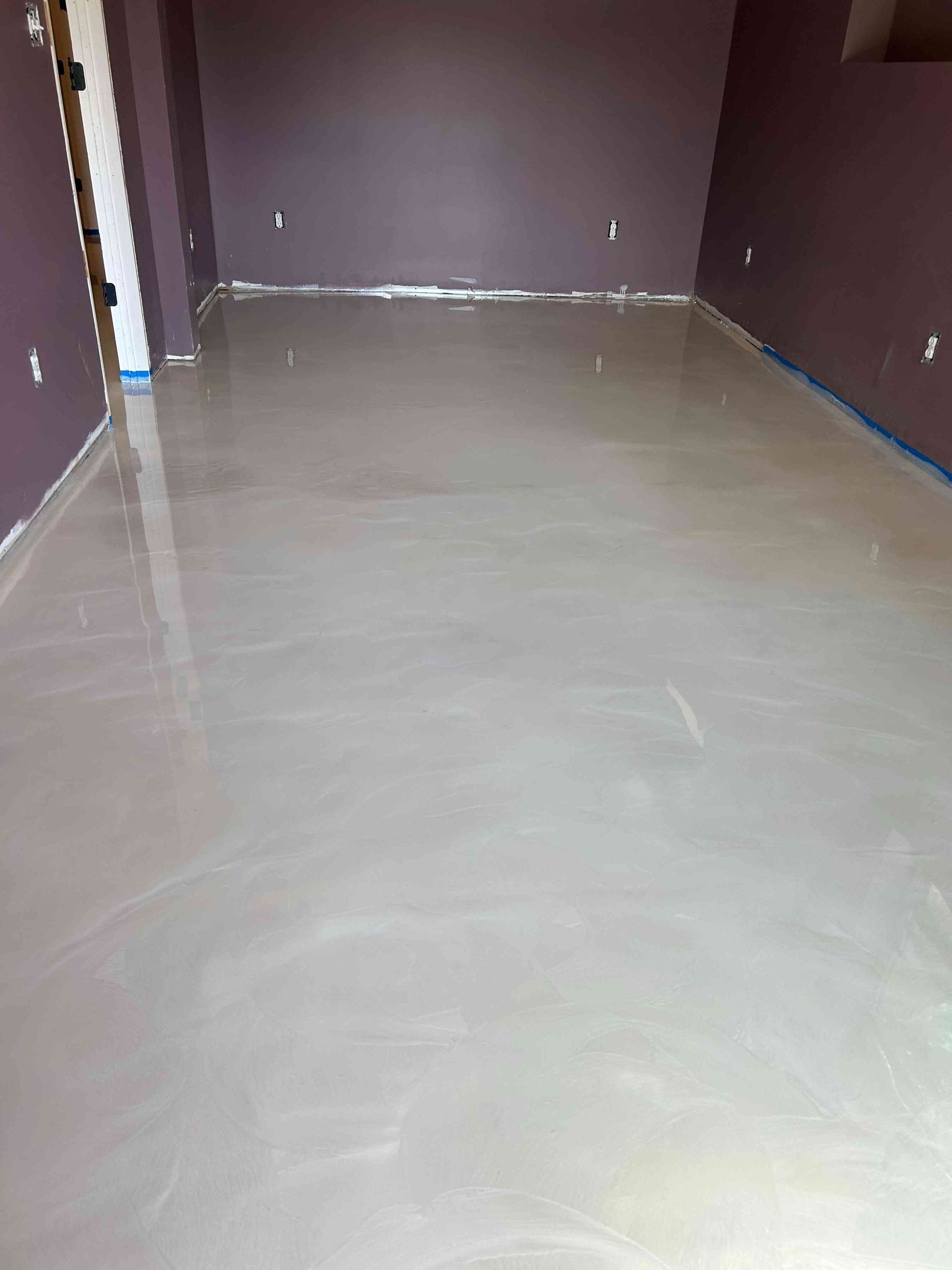 Room with newly installed, glossy, light-colored, epoxy floor. Purple walls, blue tape at the edges.