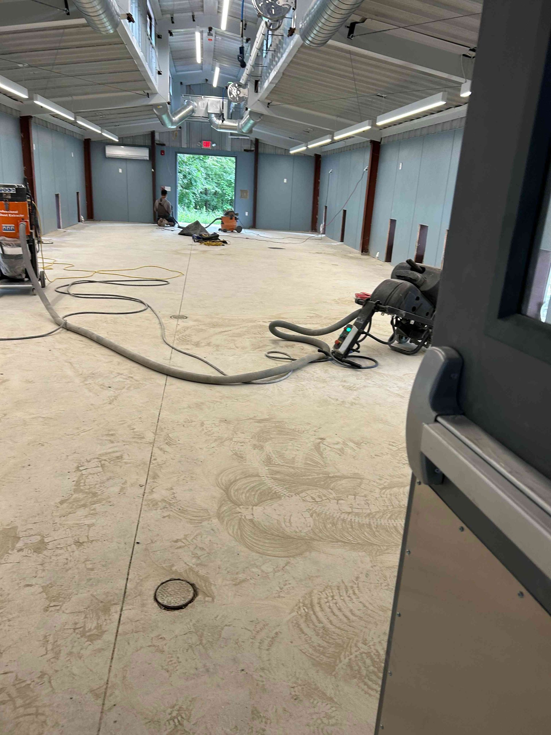 Interior of a construction site; concrete floor, workers, open doorway.