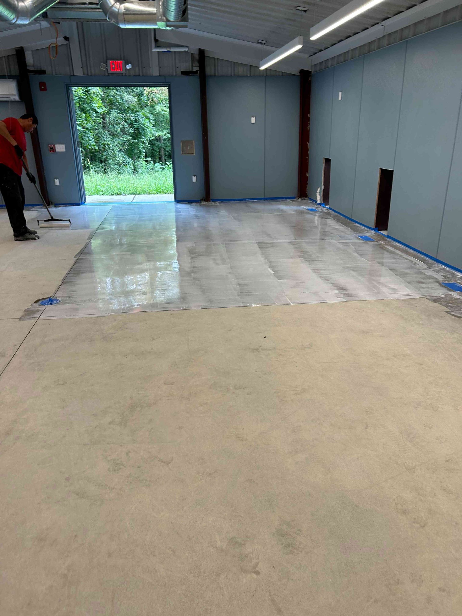 Person using a tool to smooth out a shiny concrete floor in a large, open-door interior.