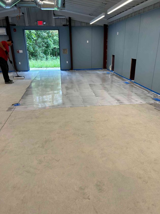 Person smoothing wet concrete in an open doorway, interior shot. Gray walls, unfinished floor.