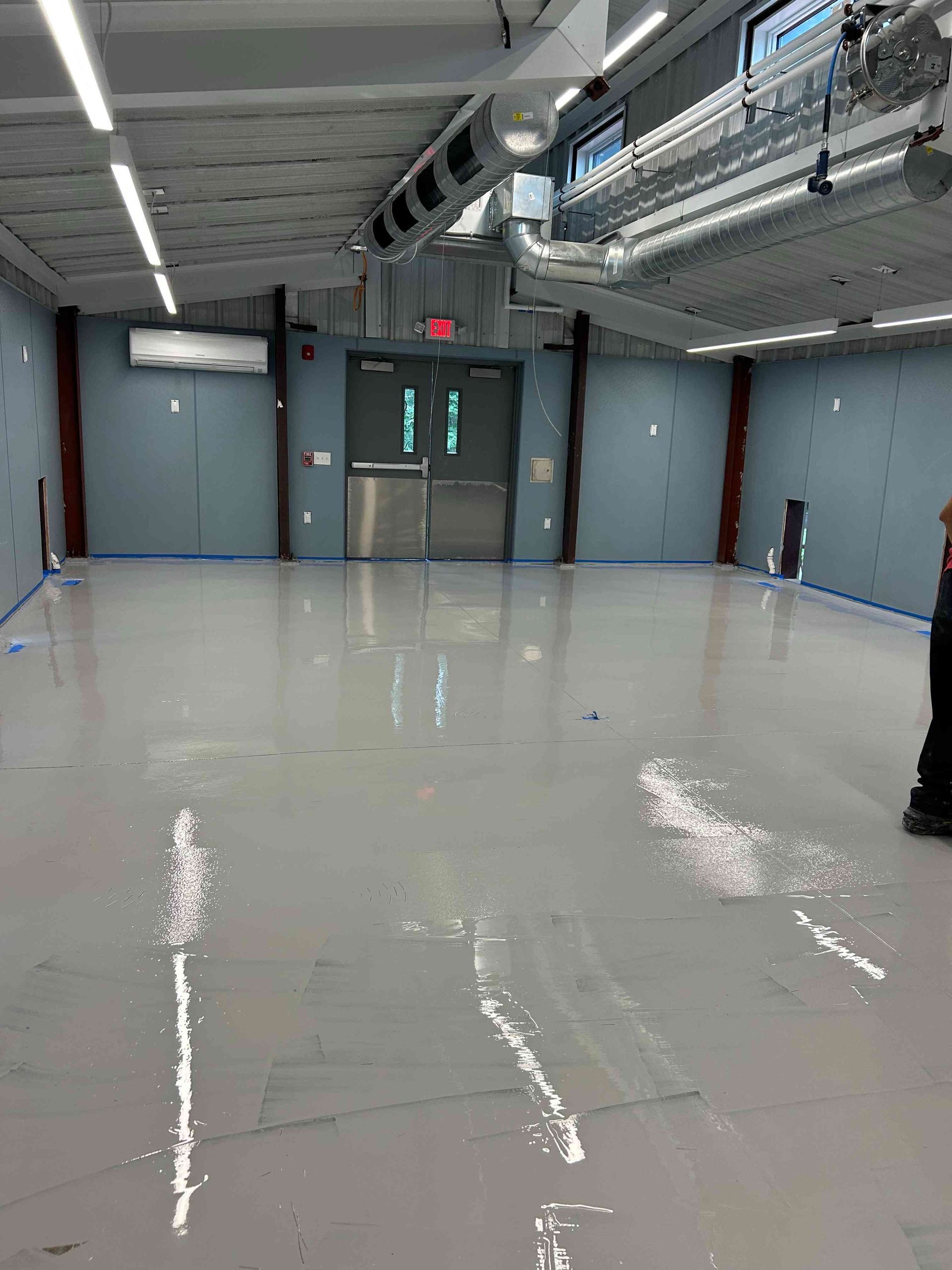 Empty, light-floored room with double doors at the far end; overhead lighting and vents visible.