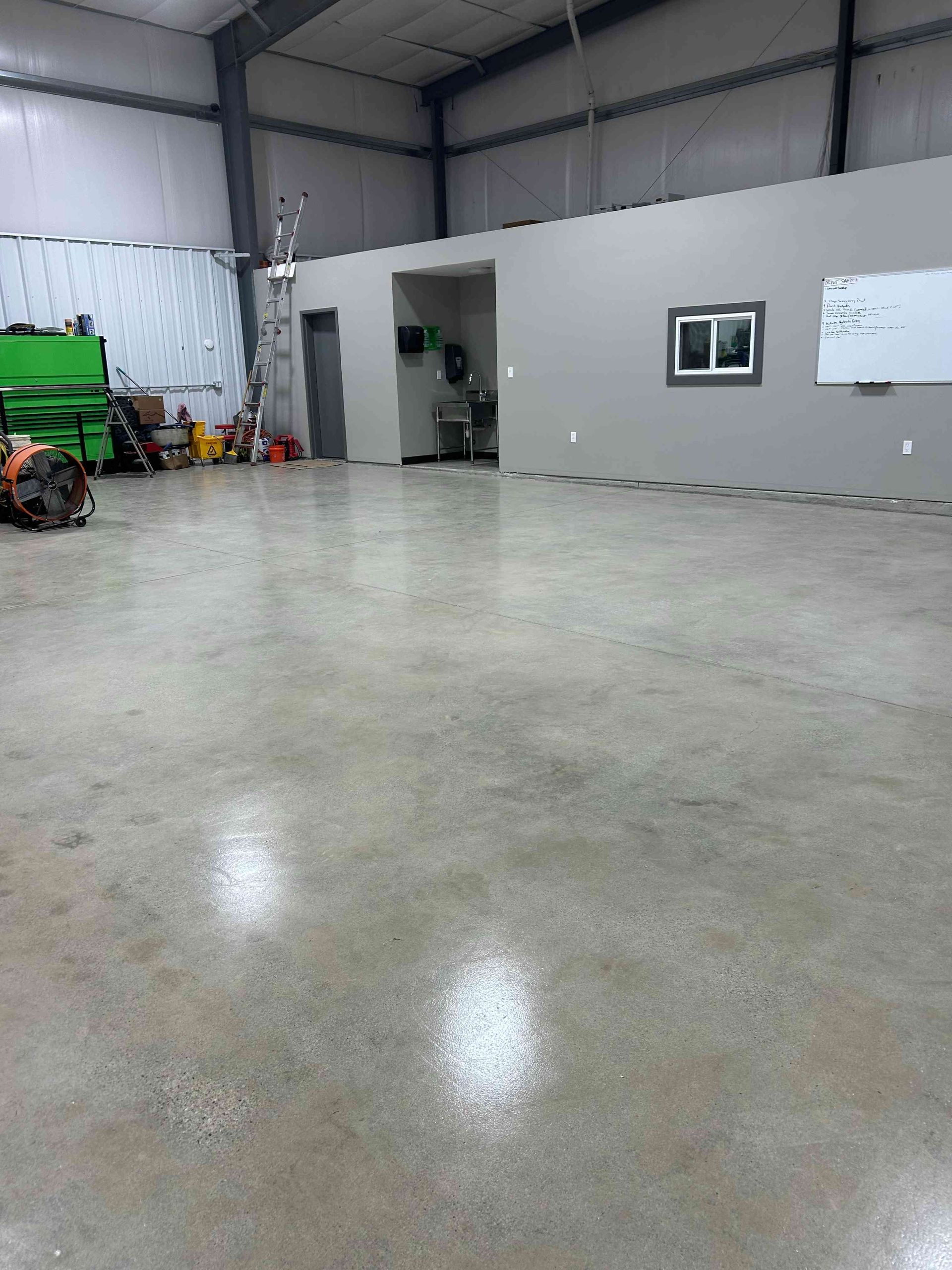 Shiny concrete floor in a large, empty industrial space with gray walls and equipment in the background.