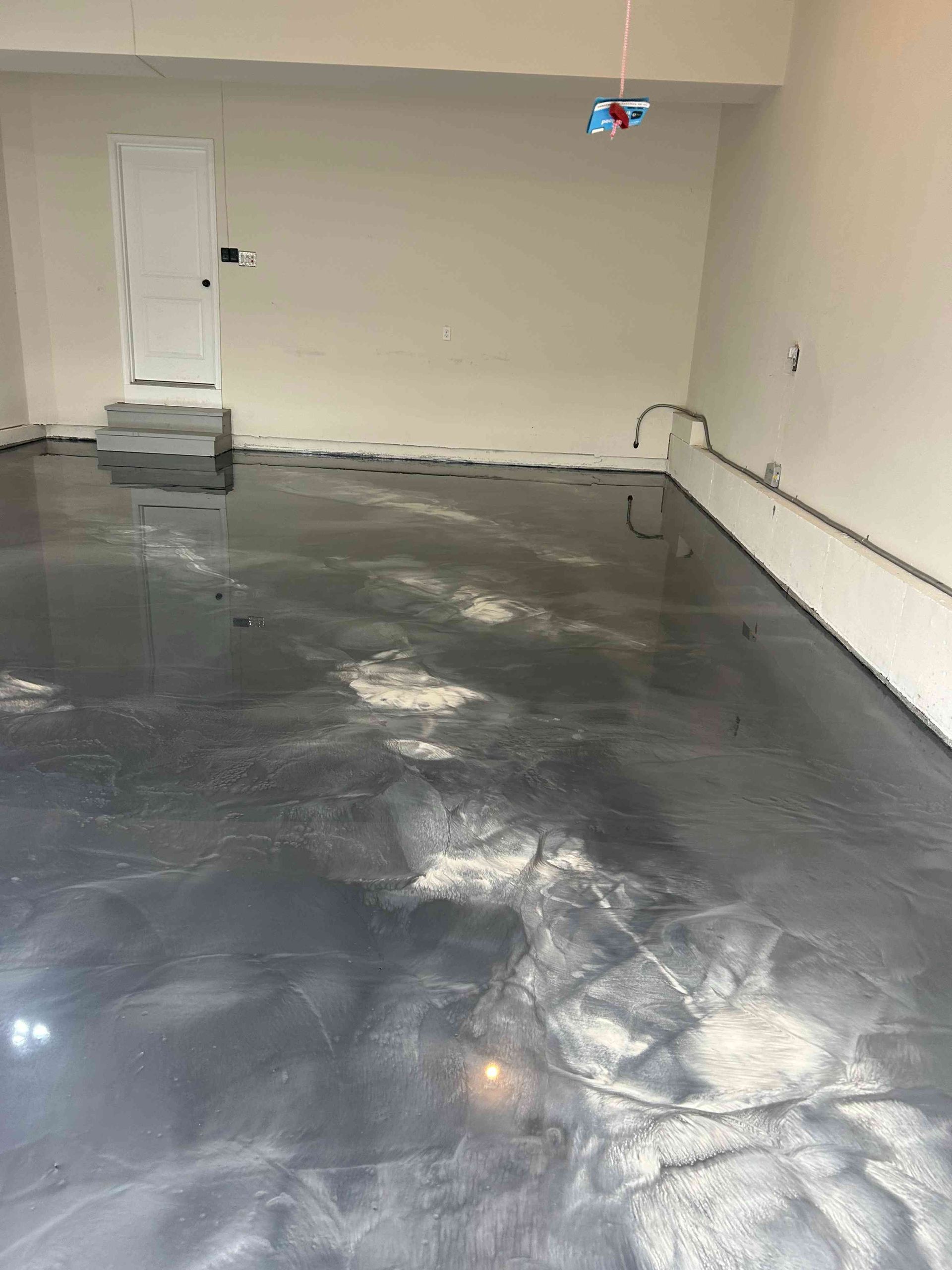 Garage with dark, glossy epoxy floor, light walls, a door, and some electrical wiring.