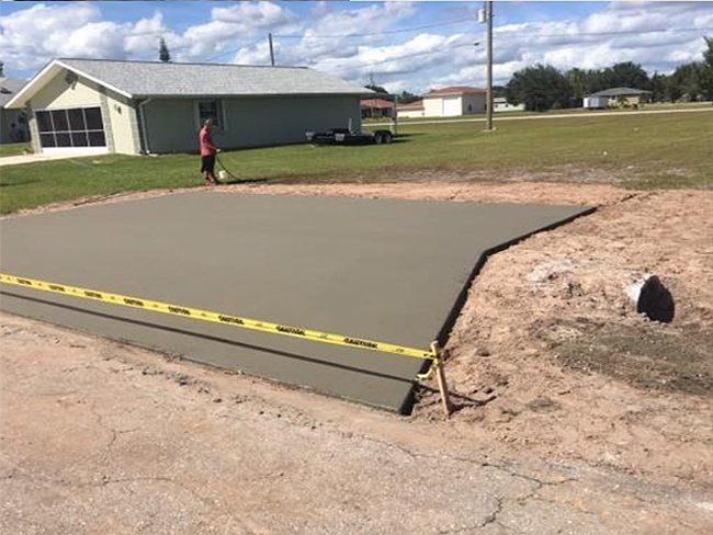 Newly poured concrete driveway with caution tape, adjacent to a house. A person is sweeping nearby.