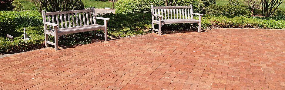 Two wooden benches sit on a brick patio in a garden setting.