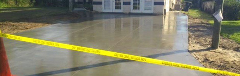 A wet concrete driveway with yellow caution tape, building in the background.