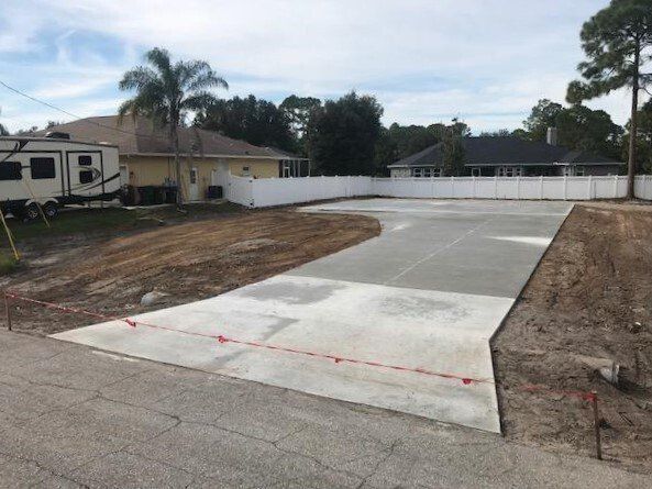 Concrete driveway with white fence in a residential setting.