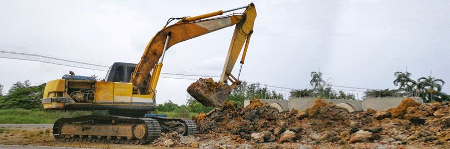 Yellow excavator digging up soil in an overcast, outdoor setting.