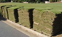 Stacks of freshly cut sod on a concrete curb, with a grassy hill in the background.