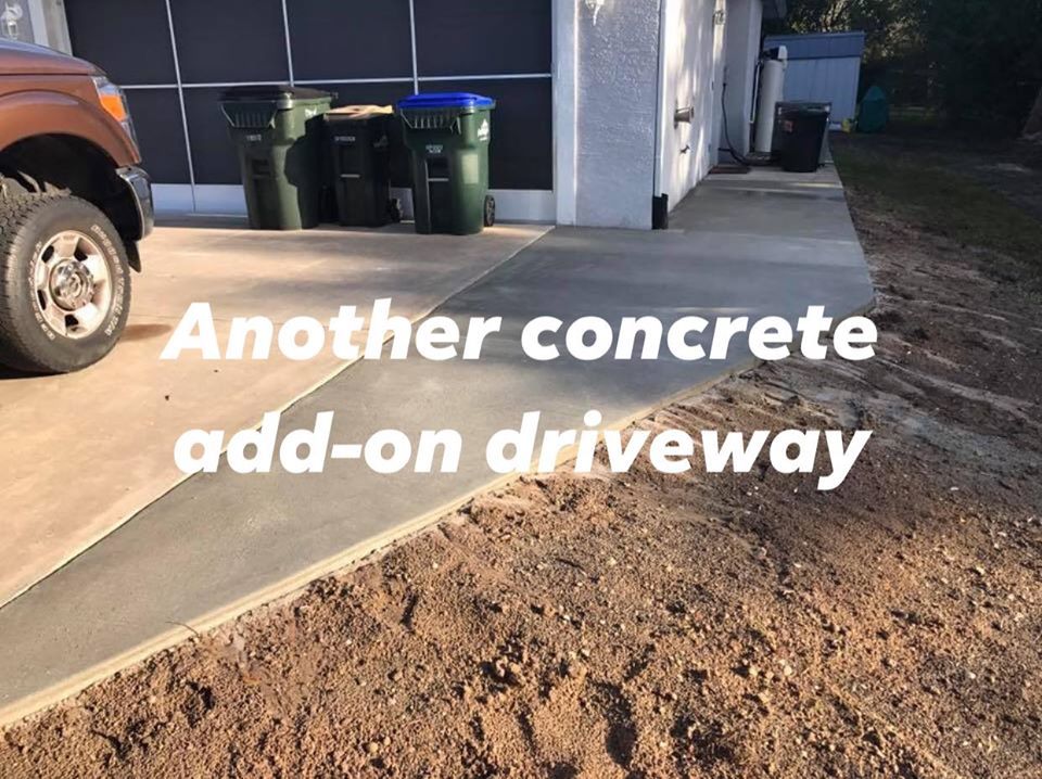 Concrete driveway addition next to a garage. A truck's tire is on the existing driveway. Trash cans are in the background.