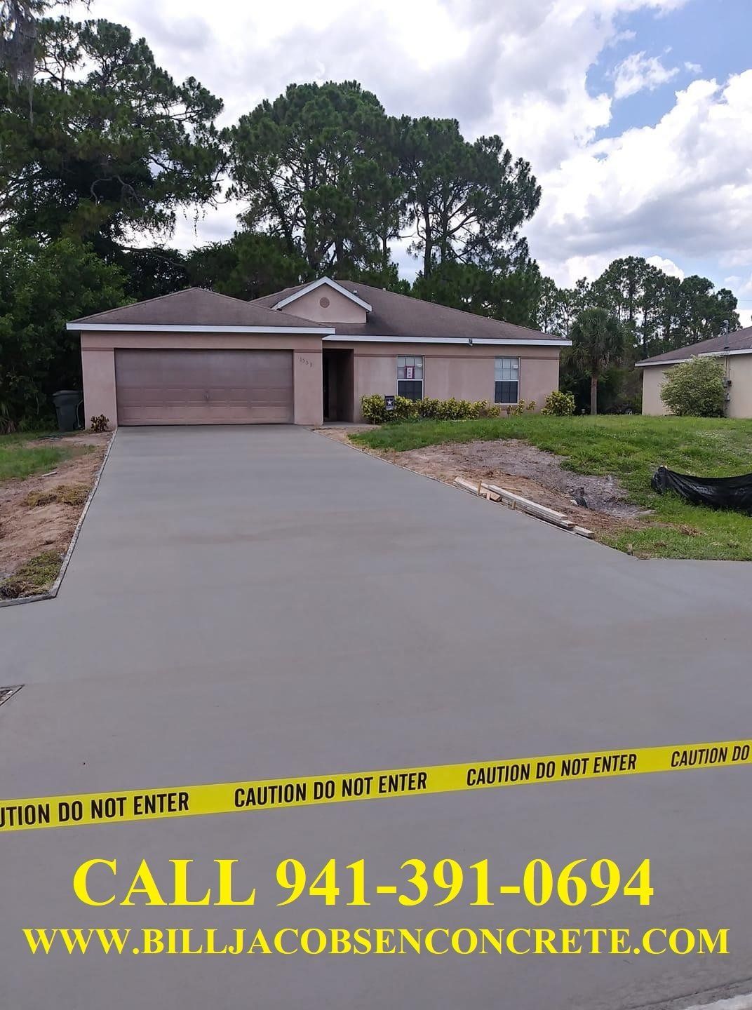 Newly poured concrete driveway in front of a tan house. Yellow caution tape and contact information are in foreground.