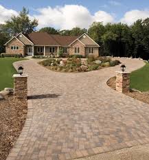Paver driveway leading to a house with a split entrance, featuring stone pillars and landscaping.