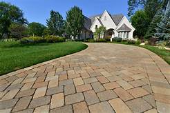 Driveway leading to a house with a green lawn. Brick pavers in tan, brown, and grey.