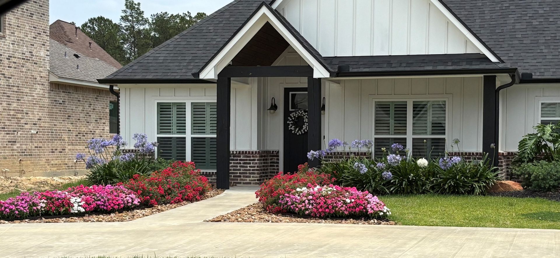Single-story suburban house with white trim, dark roof, and pink flower beds in front yard