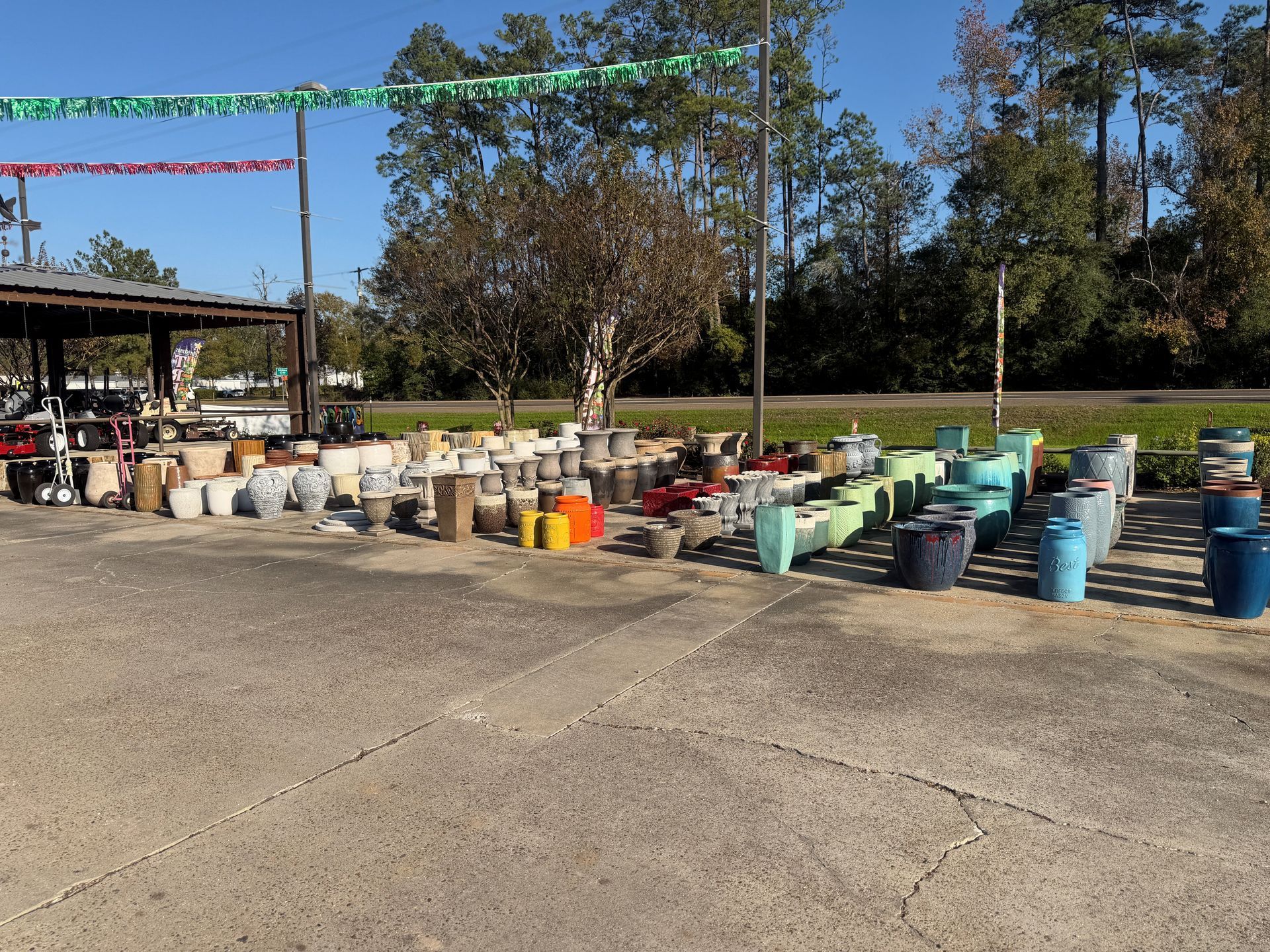 Outdoor display of various colorful plant pots for sale on a concrete surface.