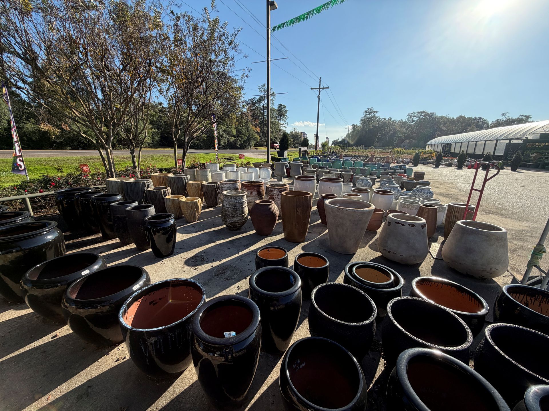 Rows of various pottery pots, in shades of black, brown, and tan, for sale outdoors on a sunny day.
