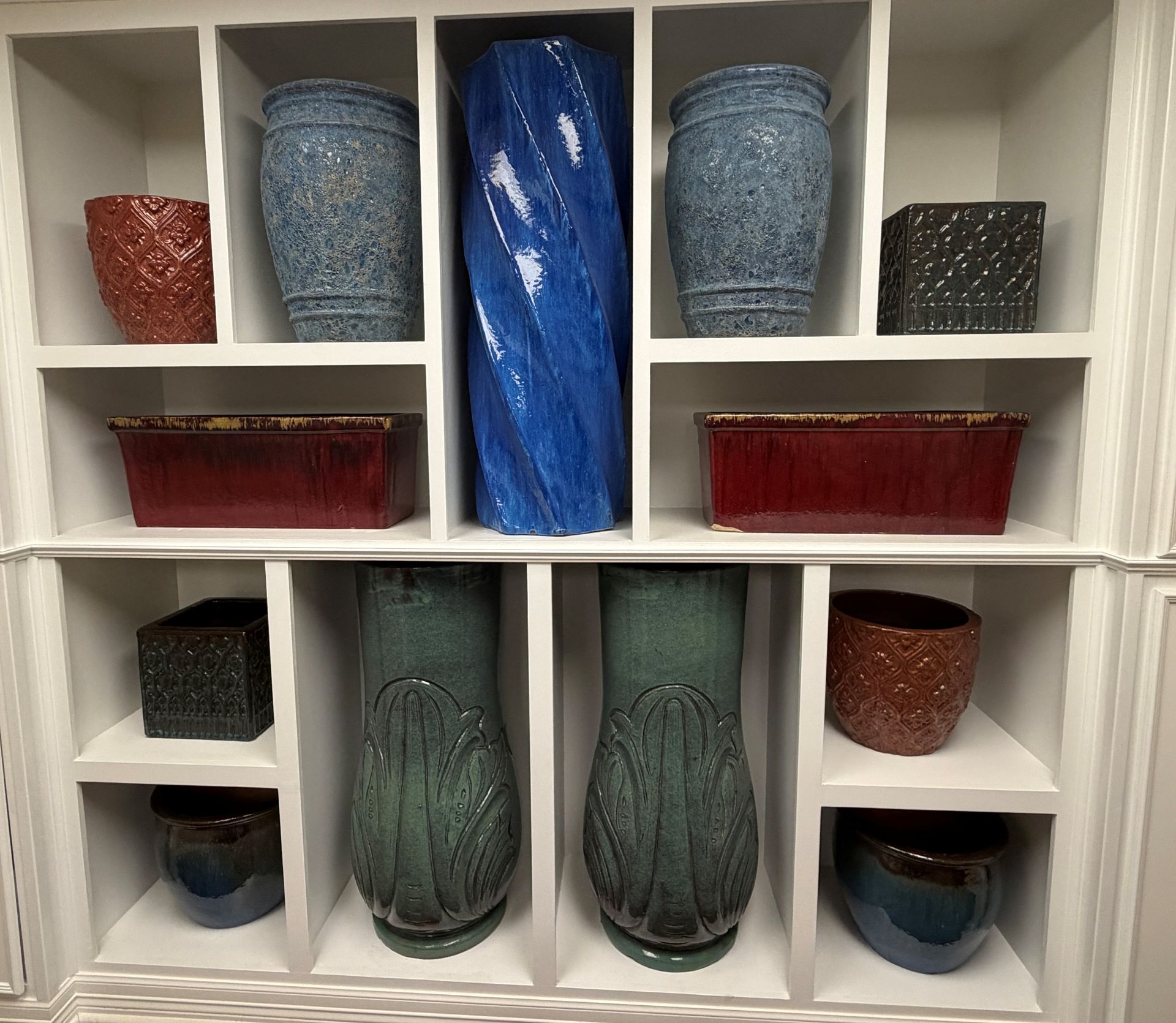 Various ceramic planters in white shelving unit; blue, red, and green tones.