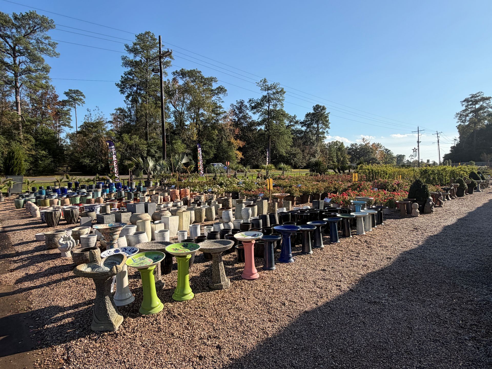 Outdoor shot of a plant nursery. Rows of bird baths, planters, and pottery are displayed on gravel.