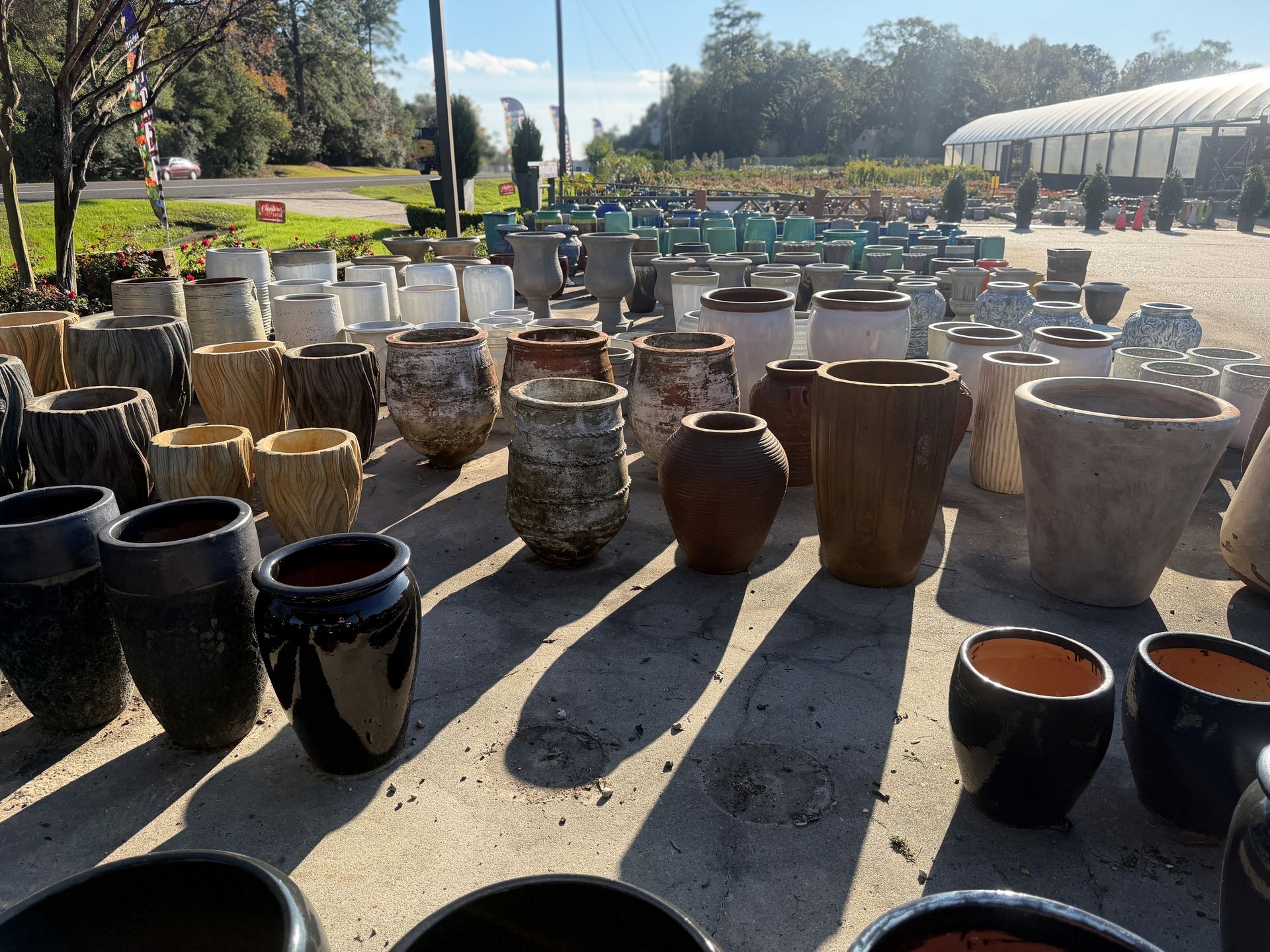 Rows of various ceramic pots for sale in an outdoor garden center on a sunny day.