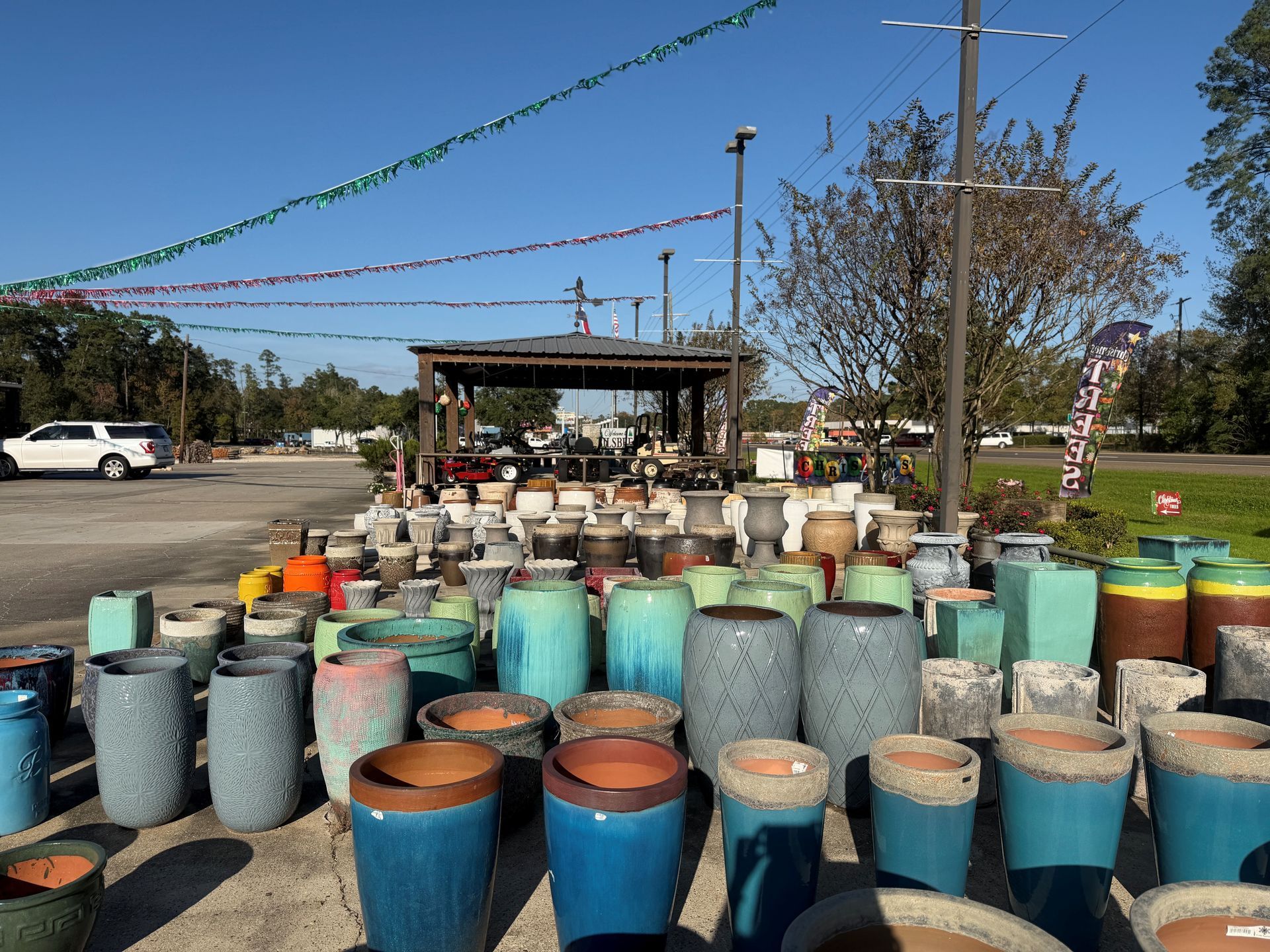 A variety of colorful ceramic planters displayed outdoors under a blue sky, some in front of a covered structure.