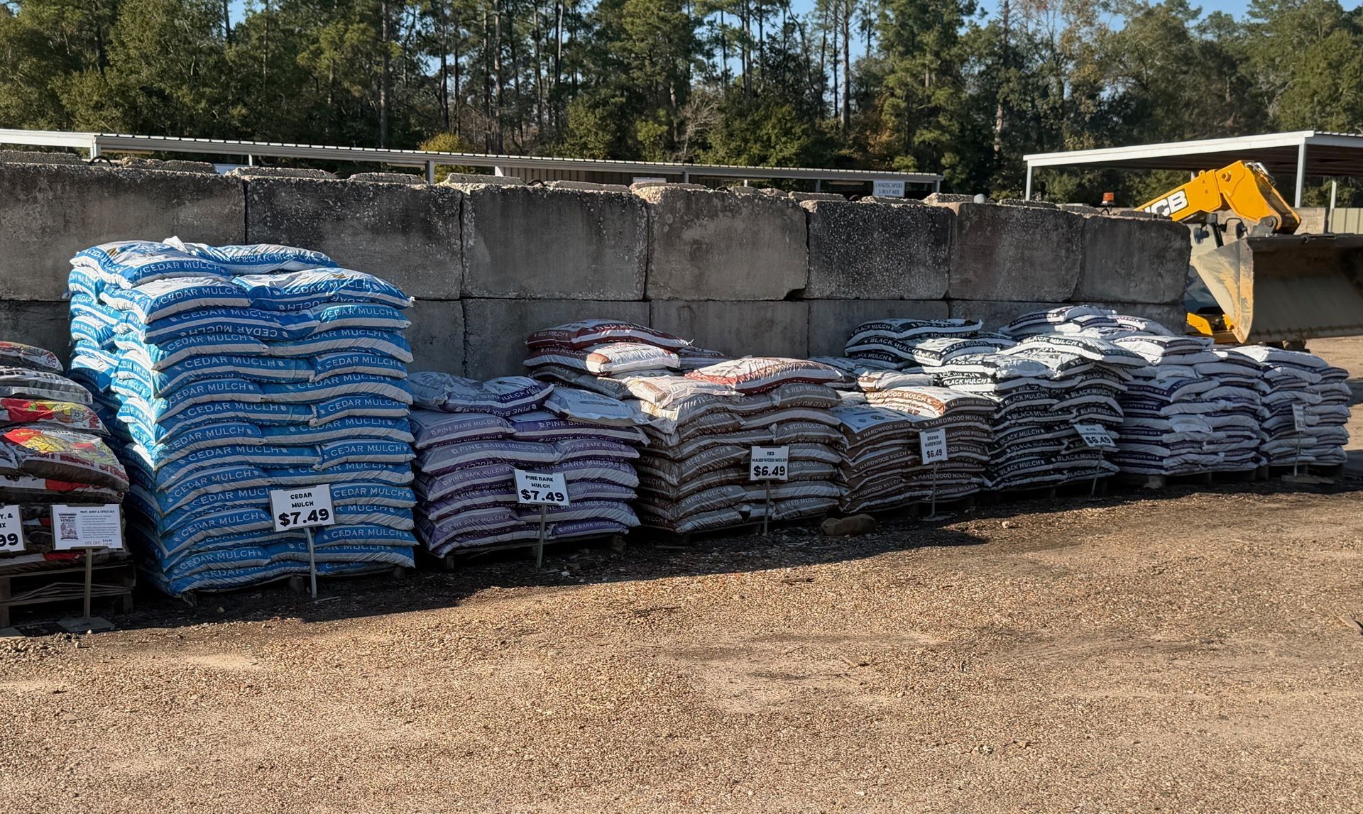 Bags of colorful gravel for sale, stacked outside, with price tags in front.