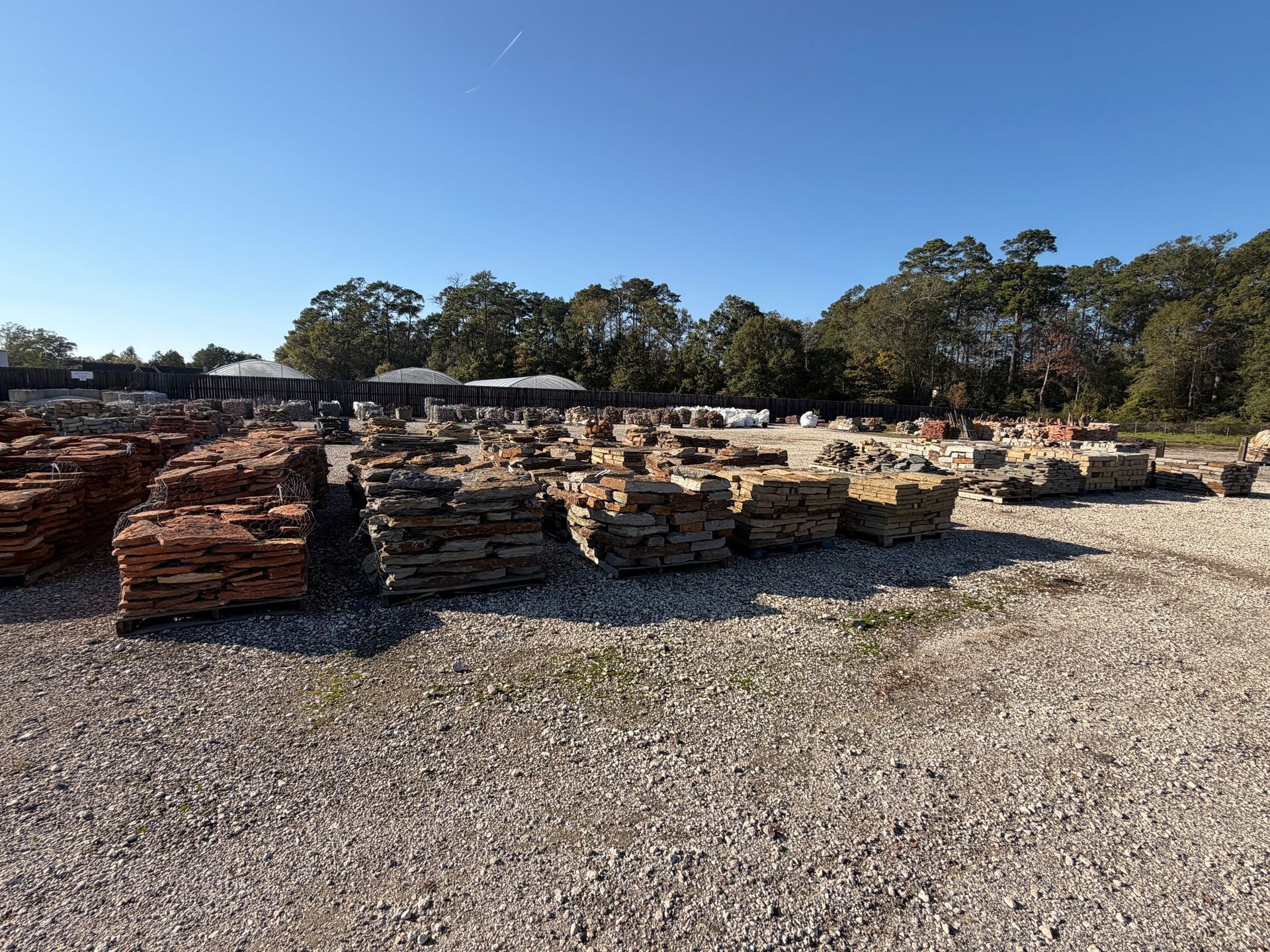 Piles of bricks and stones for sale in an outdoor yard under a clear, blue sky.