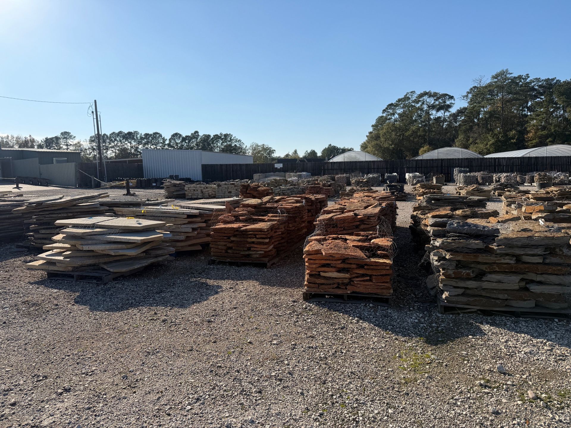 Stacks of stone slabs at an outdoor landscaping supply store, under a sunny sky.