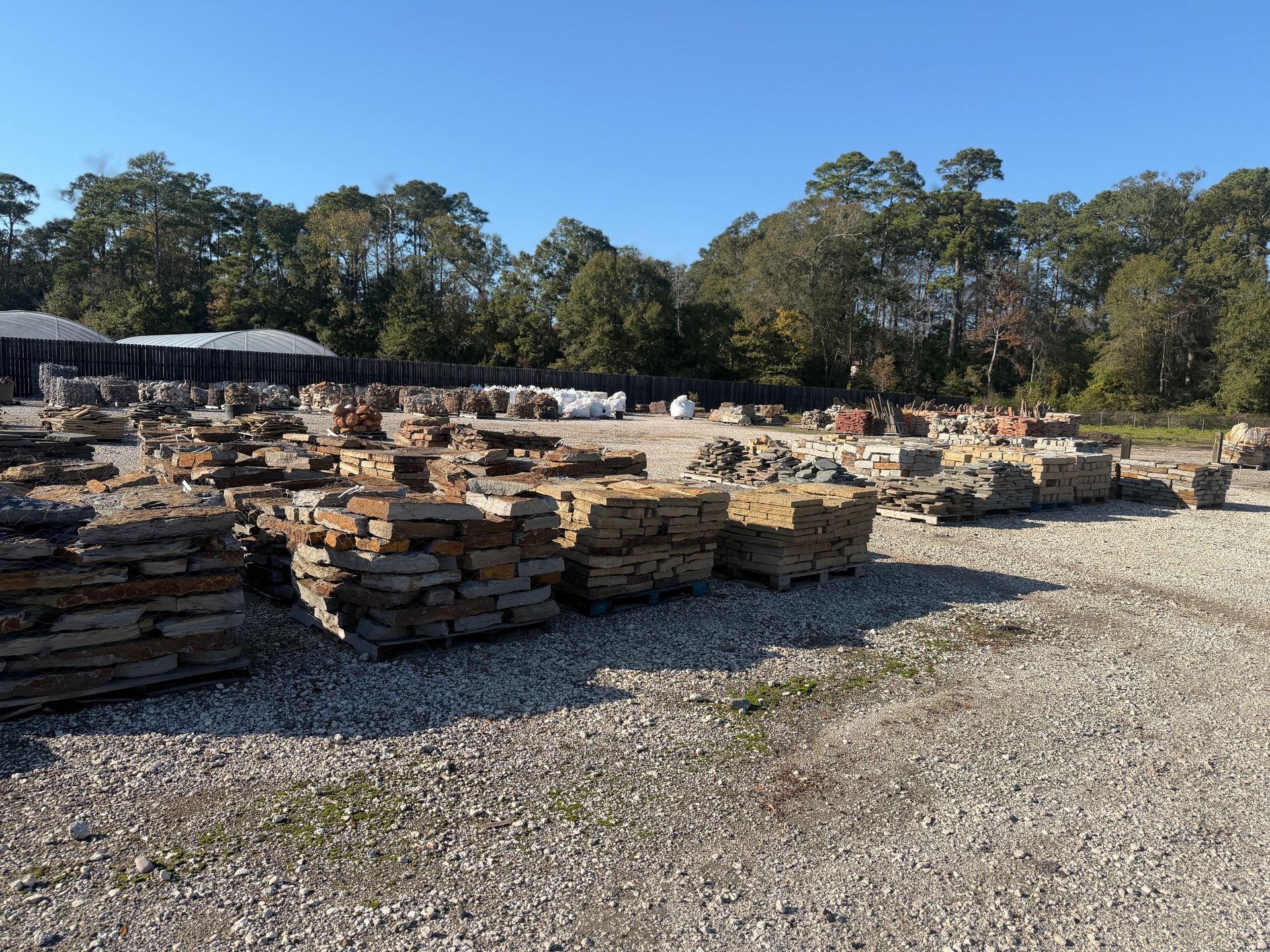 Stone pavers on pallets in an outdoor lot, trees in the background. Sunny day.
