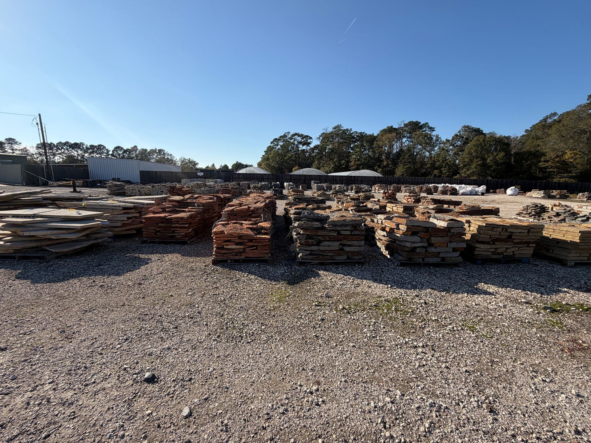 Piles of stone and brick pavers in an outdoor yard under a clear blue sky.