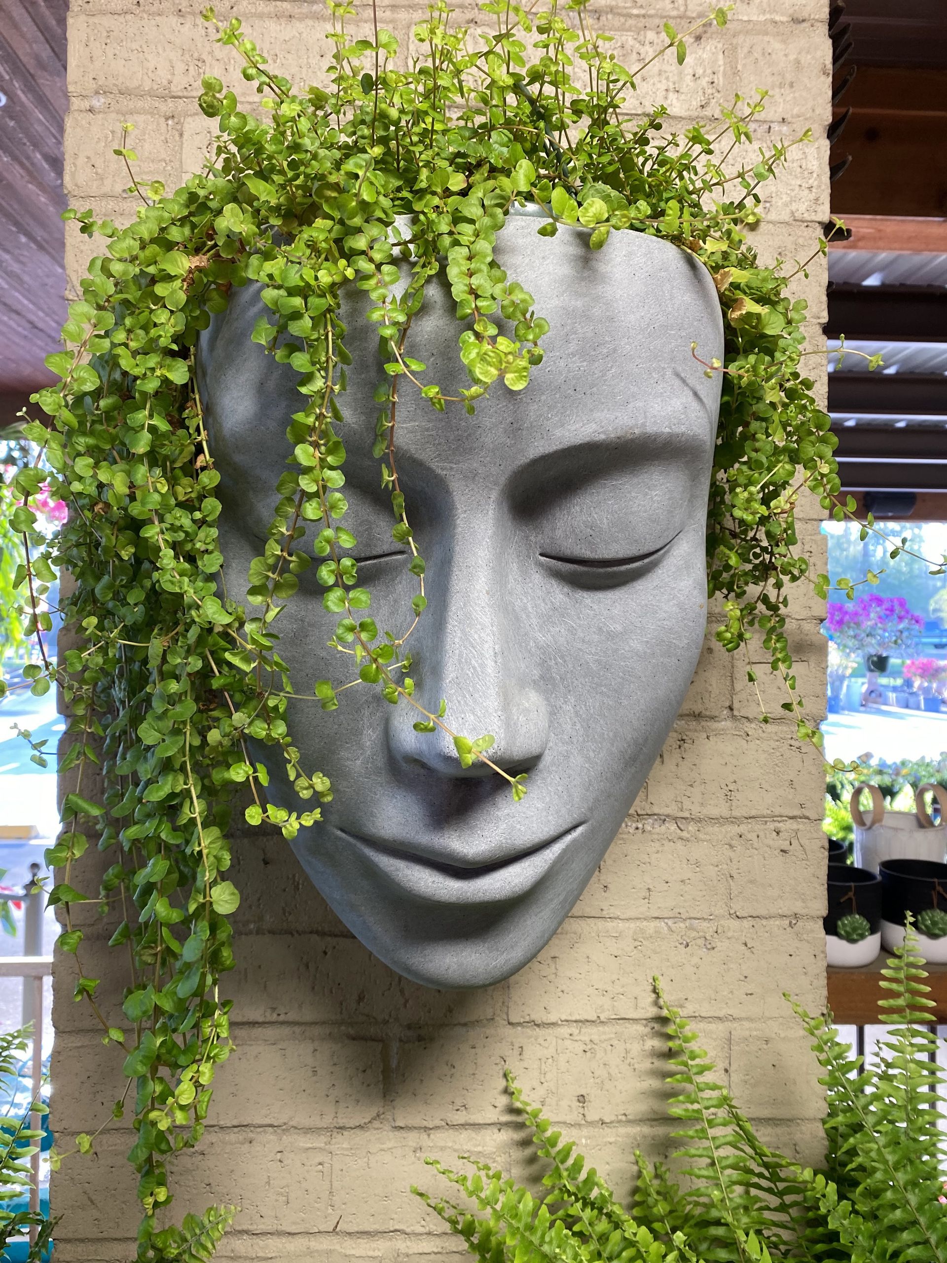 Stone face planter with cascading green foliage, mounted on a brick pillar.