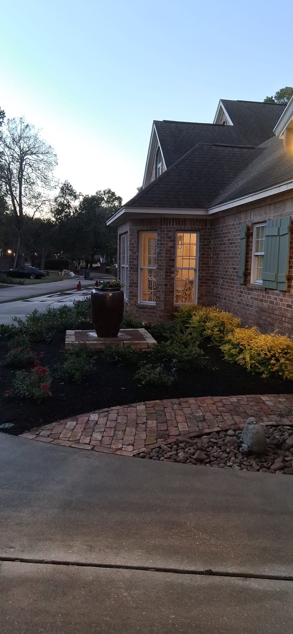 Brick house exterior at dusk with landscaping, a dark stone urn, and a brick walkway.