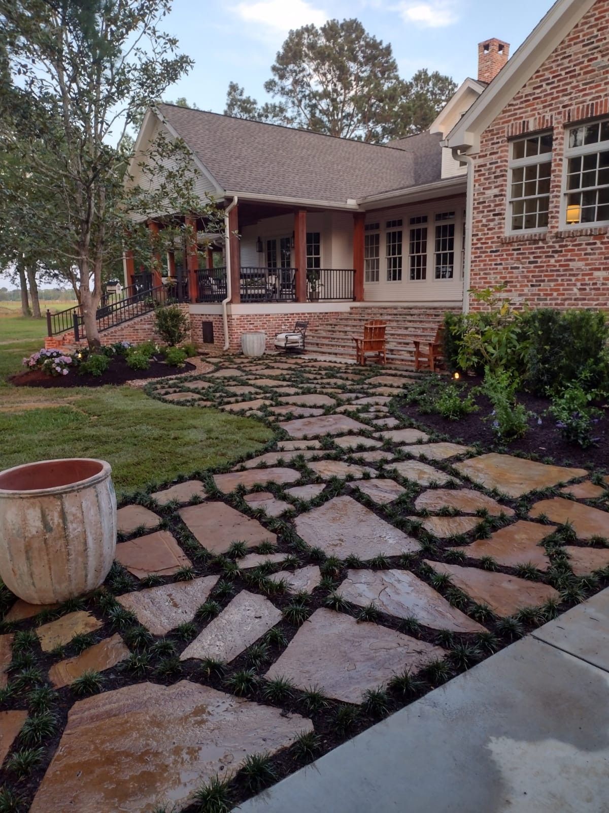 Flagstone pathway through a yard, leading to a brick house with a porch and landscaping.