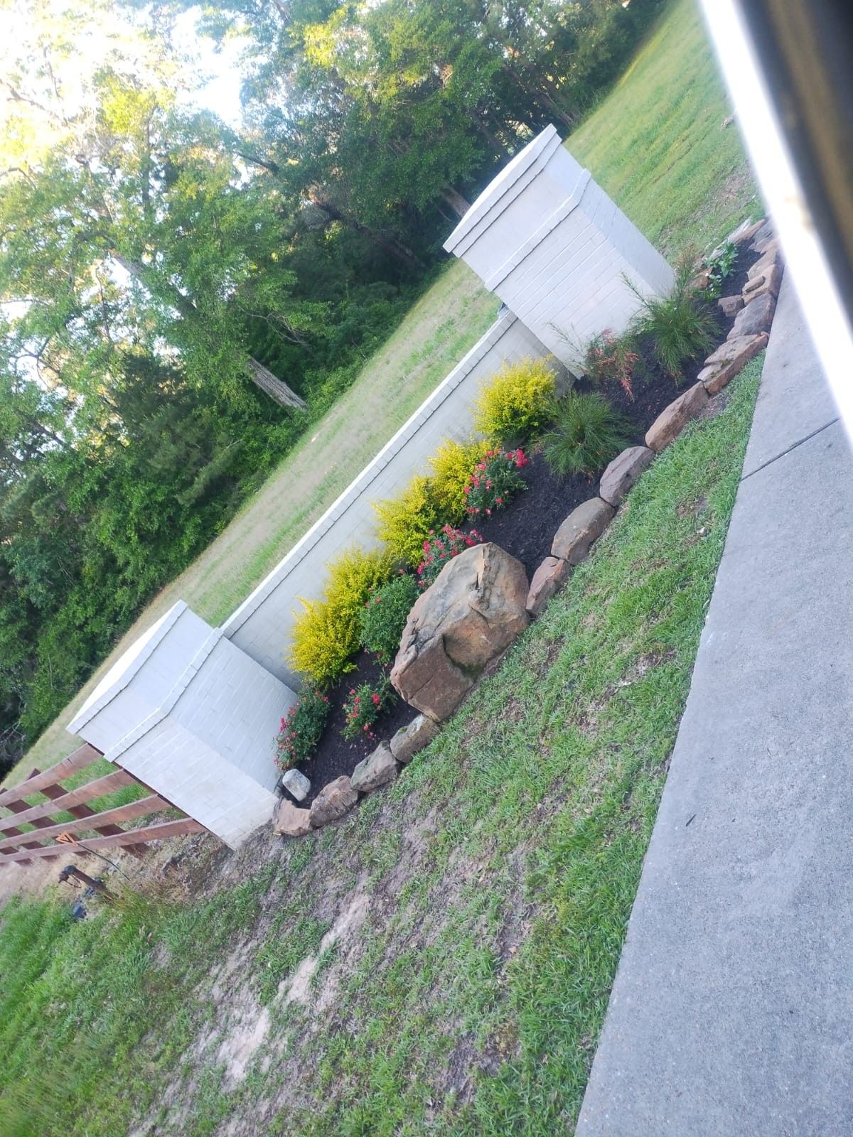 Stone retaining wall and flowerbed on a sloped lawn with white columns.