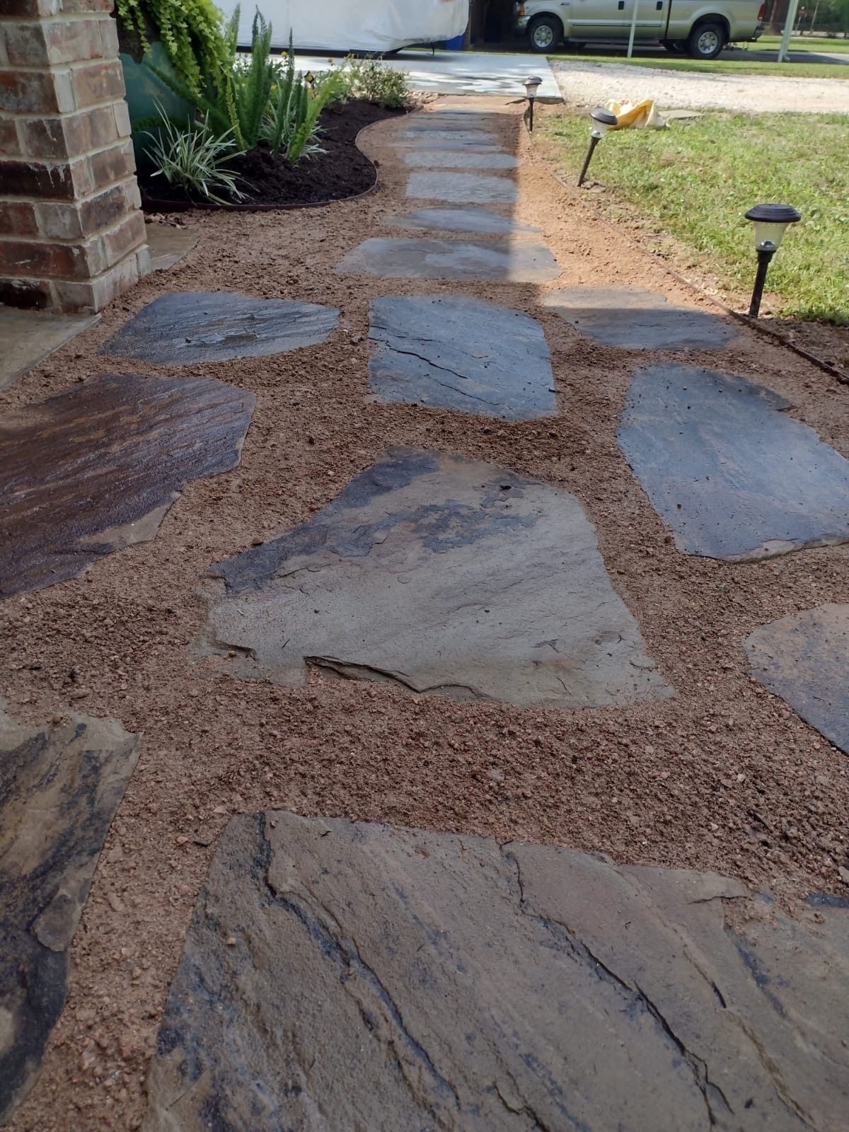 Flagstone path through gravel leading to a brick-columned porch, with a small garden bed and solar lights.