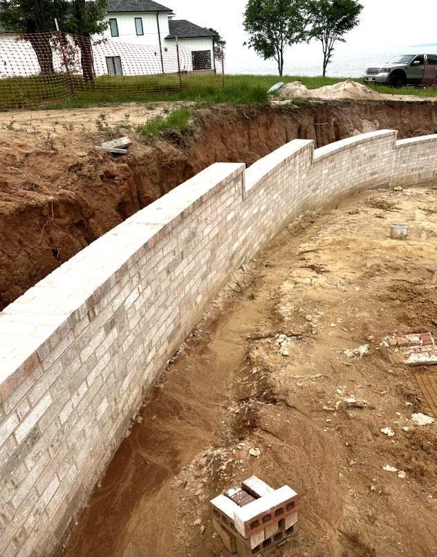 A brick wall is being built in the dirt near a house