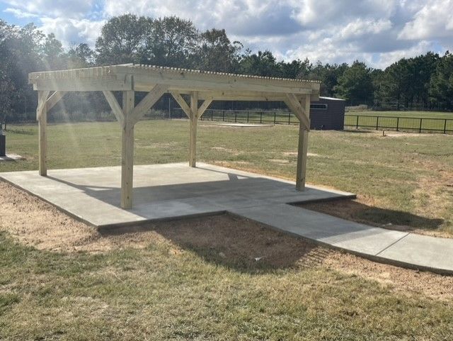 a wooden pergola is sitting on top of a concrete platform in a field .