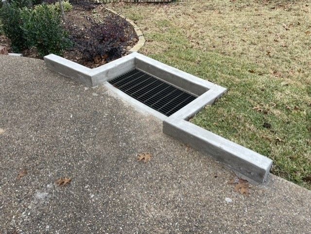 A drain on the side of a sidewalk next to a grassy area.