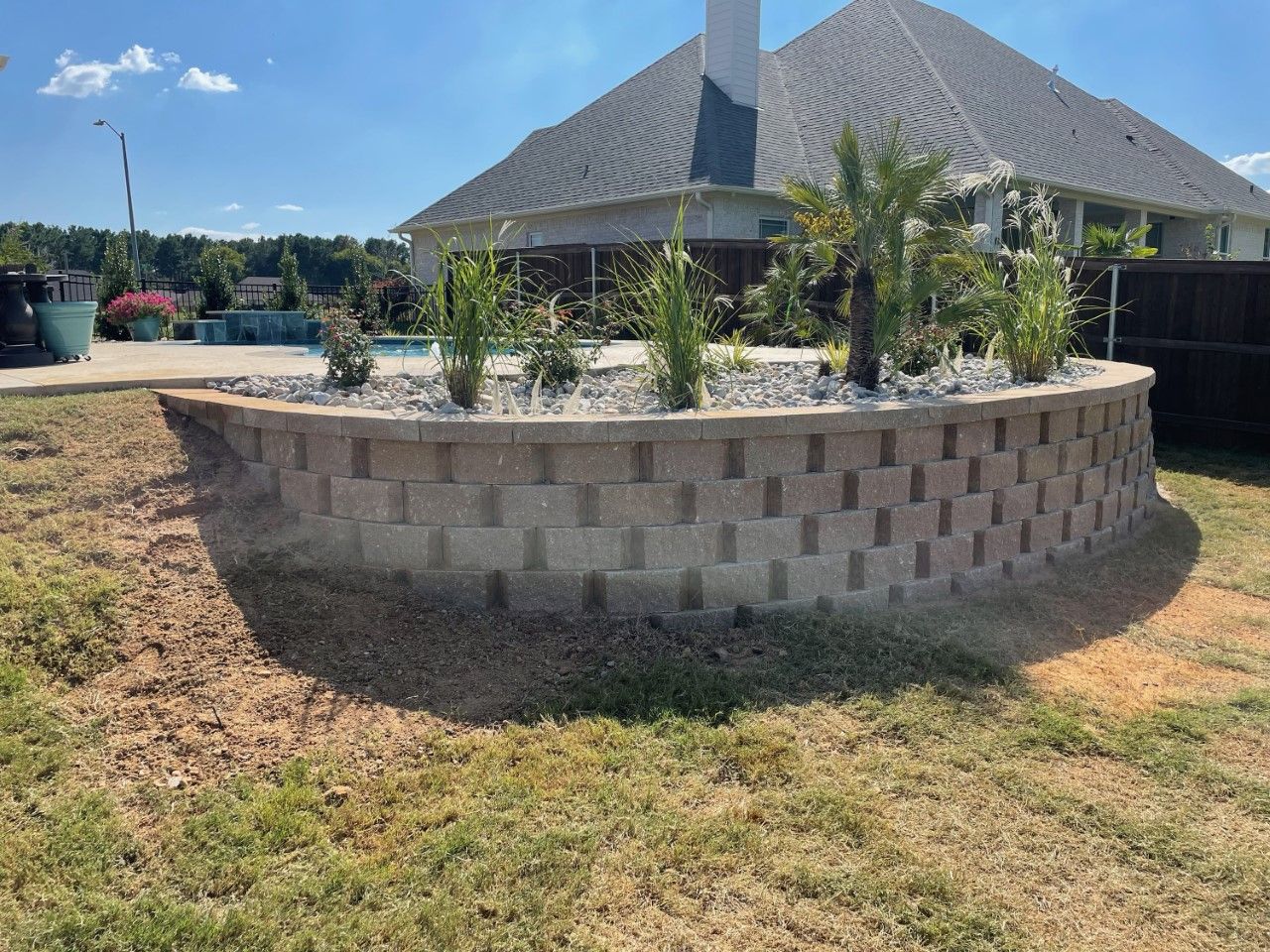 A brick wall in a yard with a house in the background.