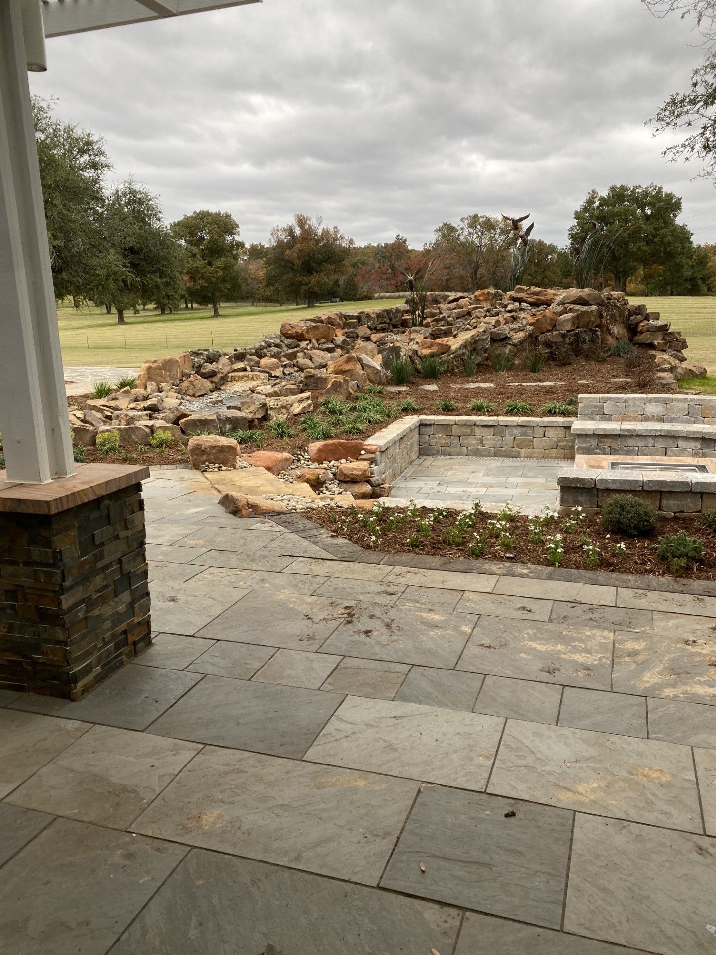 A patio with a fire pit and a large rock wall in the background.
