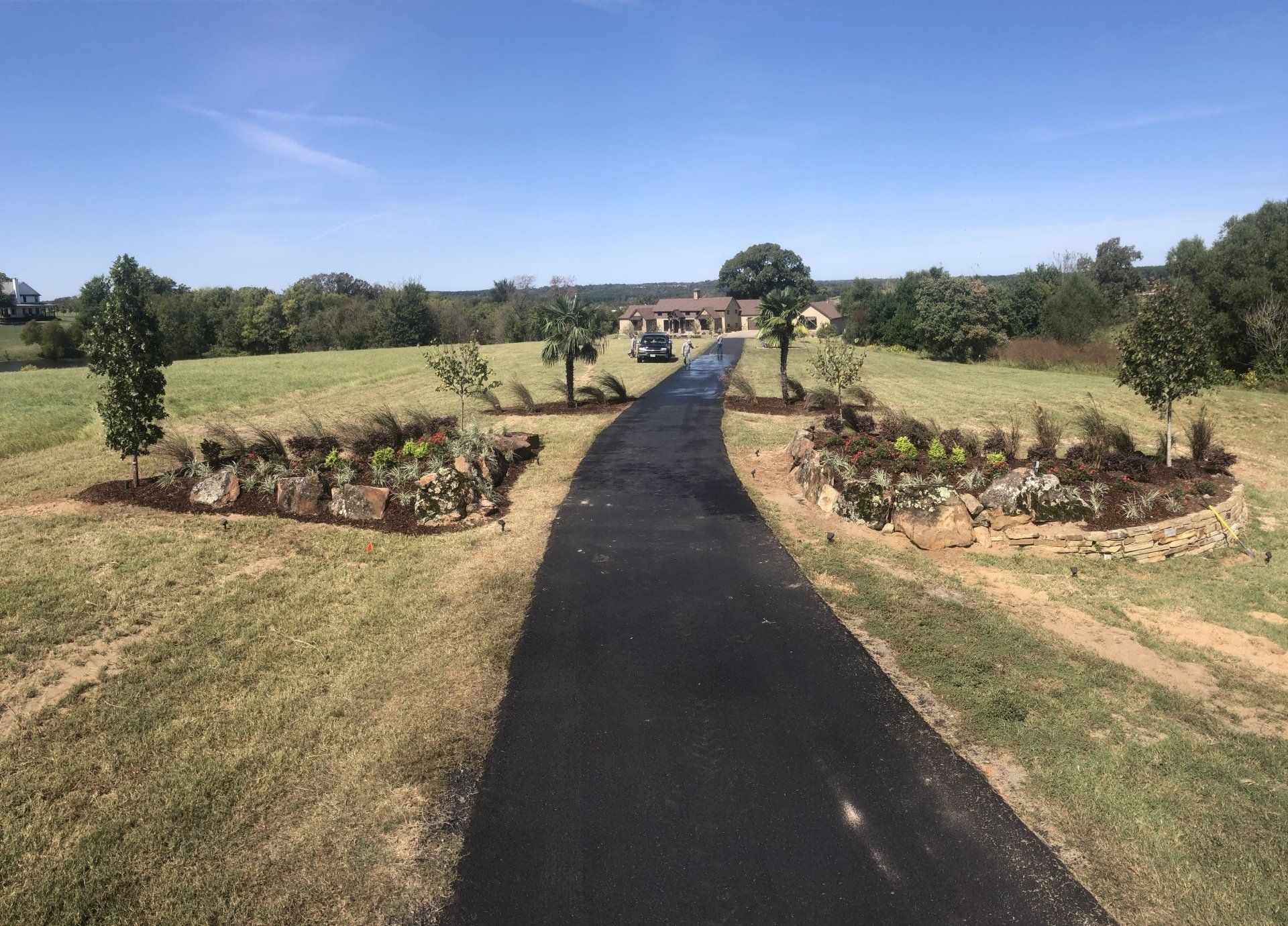 A driveway leading to a house in the middle of a grassy field.