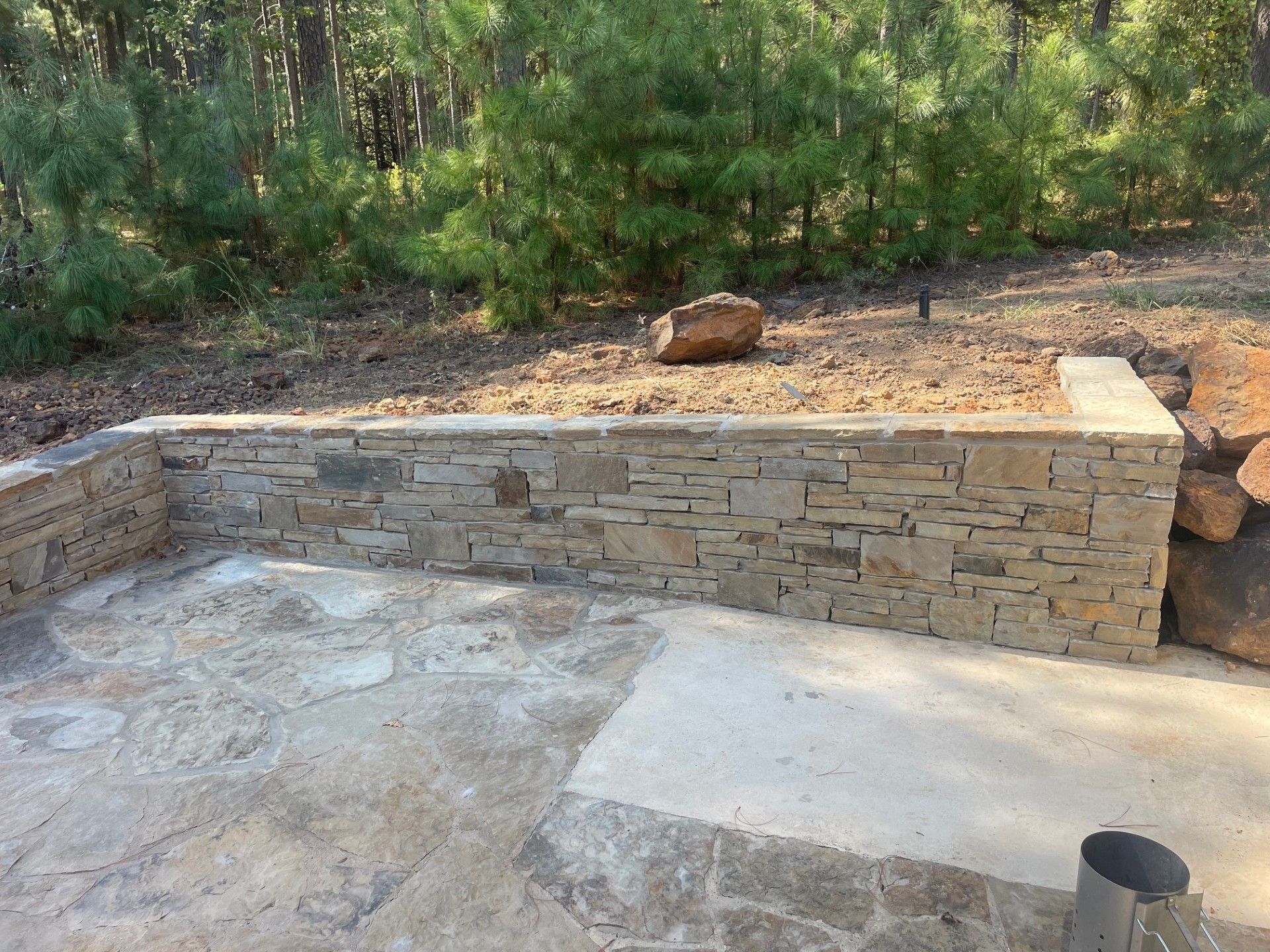 A retaining wall is surrounded by rocks and trees