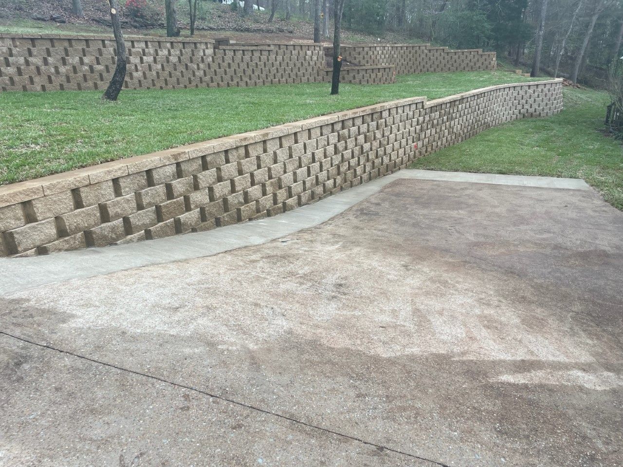 A brick wall surrounds a concrete driveway in a yard.