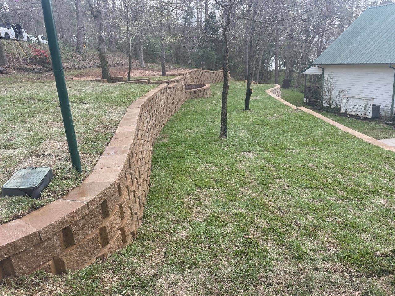 A brick wall surrounds a lush green lawn in front of a house.