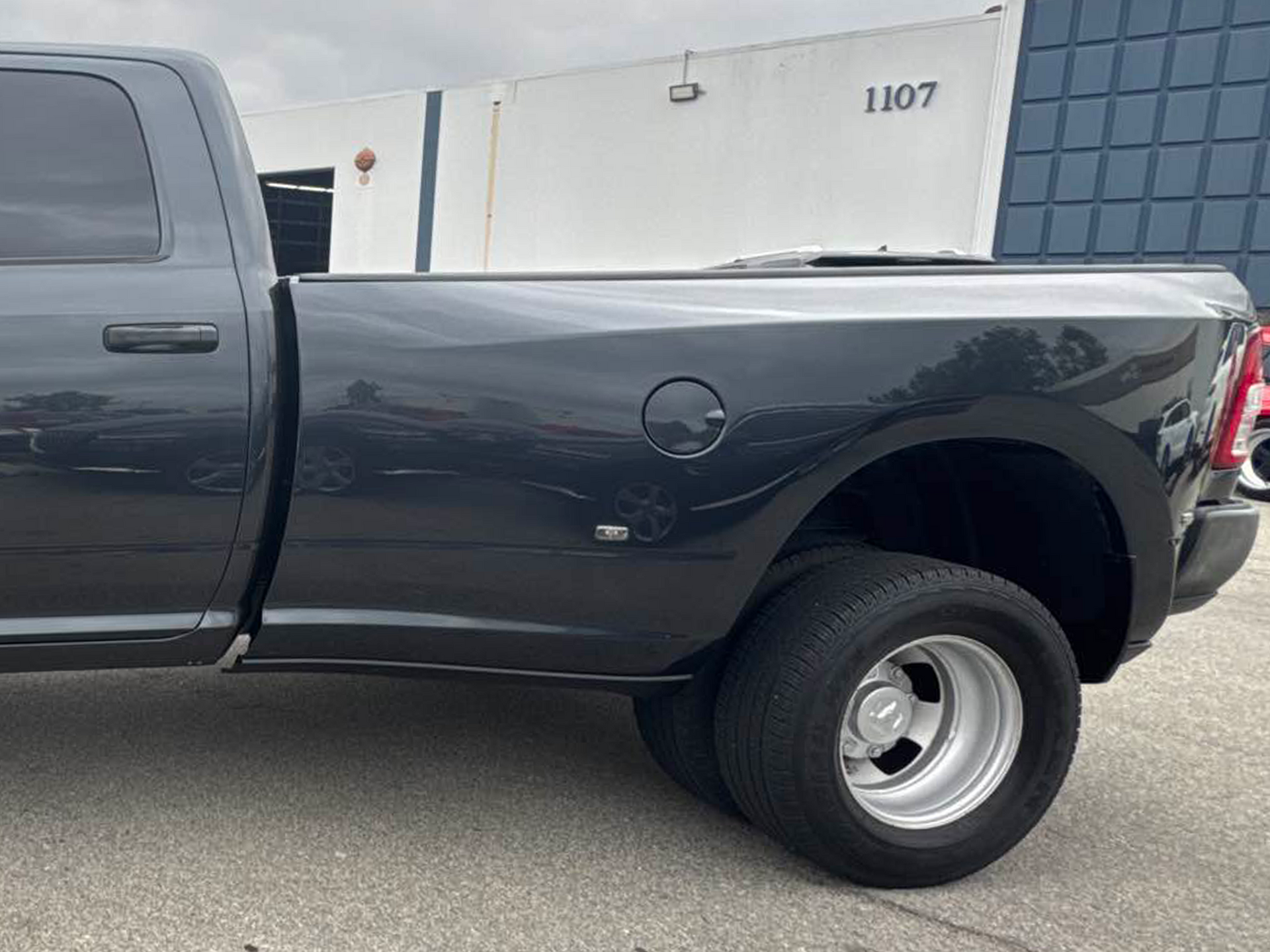 Black pickup truck parked outside a building, side view of the bed and rear wheel.