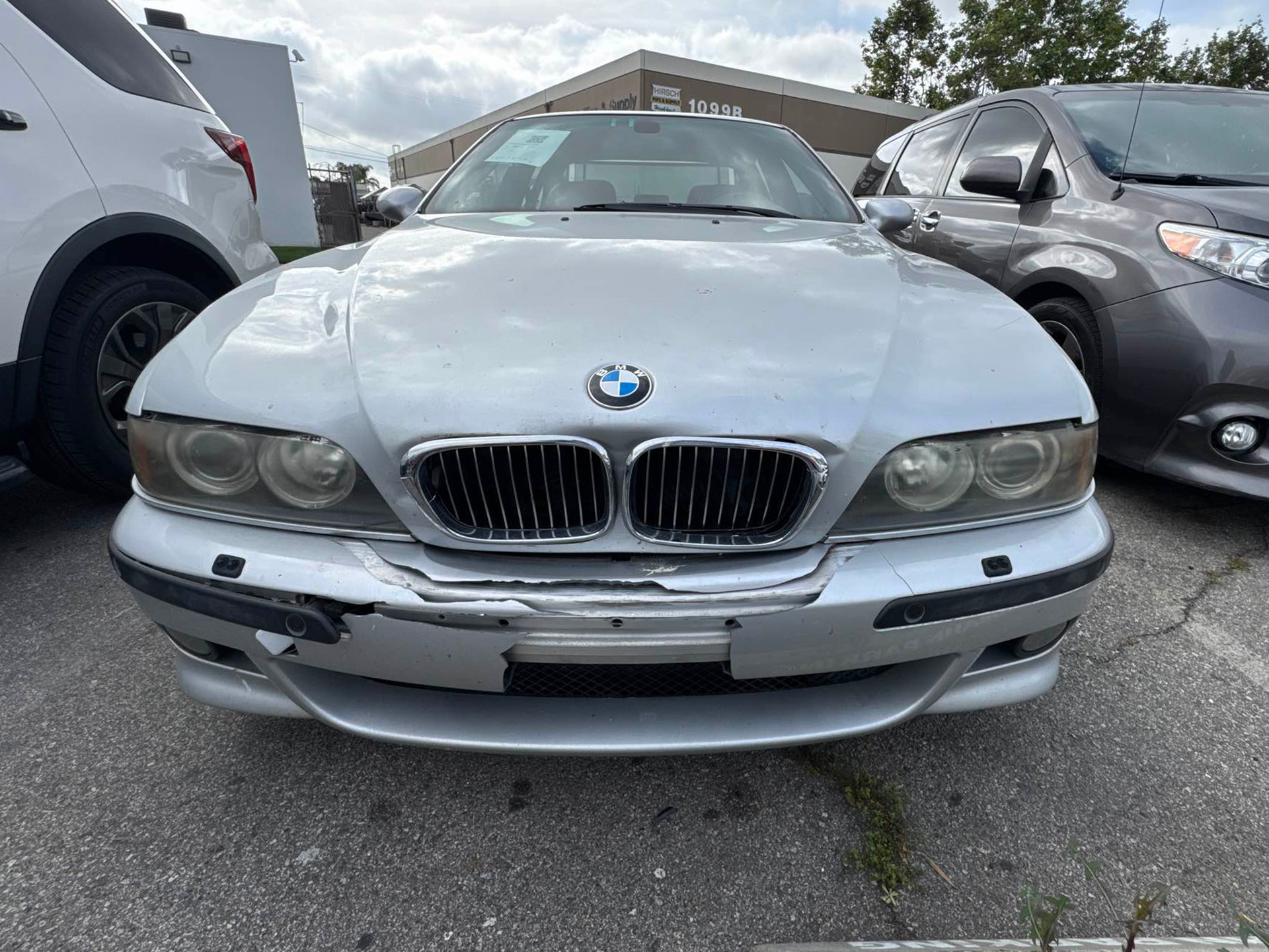 Front view of a silver BMW sedan parked between two vehicles in a lot.