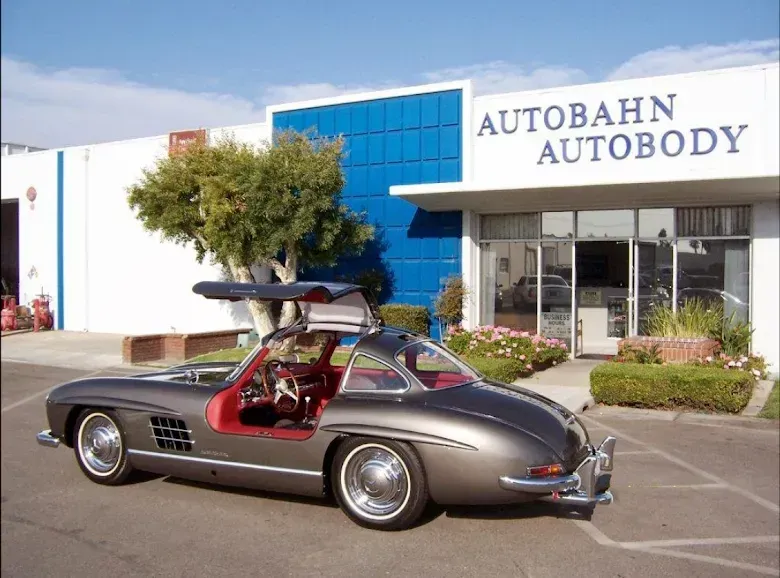 Gray Mercedes-Benz 300SL Gullwing parked outside Autobahn Autobody shop, doors open.