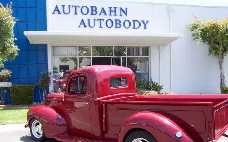 Red vintage pickup truck parked in front of the Autobahn Autobody building.