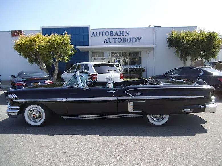 Black convertible parked in front of Autobahn Autobody; white-wall tires, sunny day.